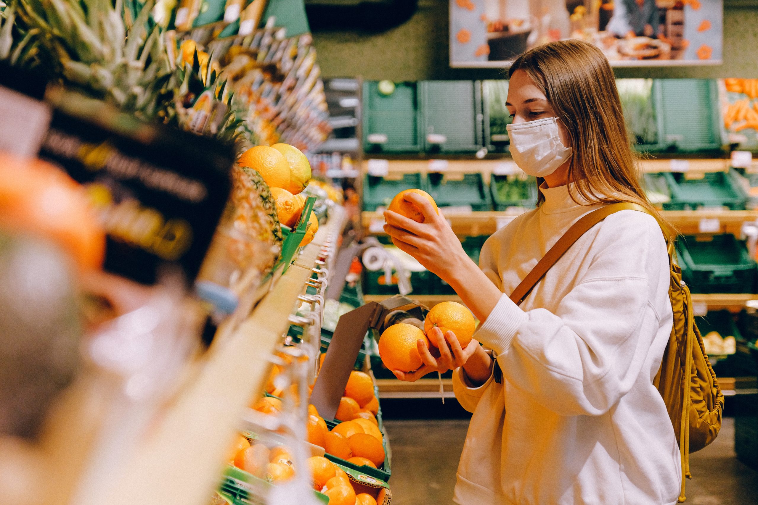 woman wearing a mask while shopping in the fresh produce section of a grocery store
