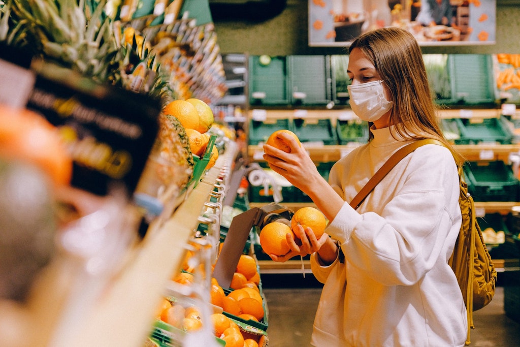 woman wearing a mask while shopping in the fresh produce section of a grocery store